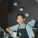Cheerful barista holding a coffee cup, smiling warmly in an Indonesian cafe.